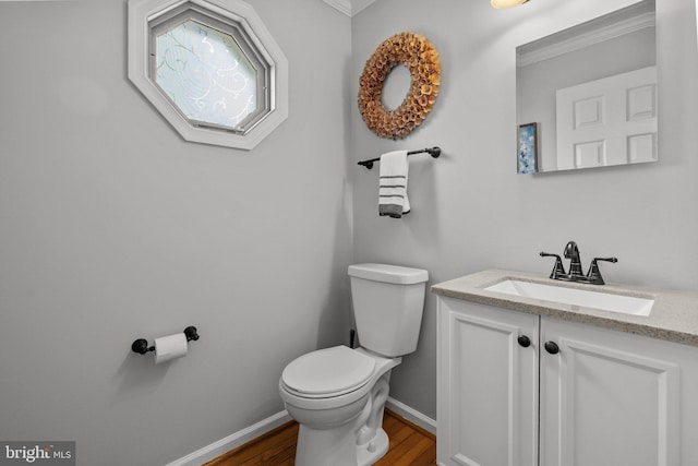 bathroom with toilet, wood finished floors, vanity, crown molding, and baseboards
