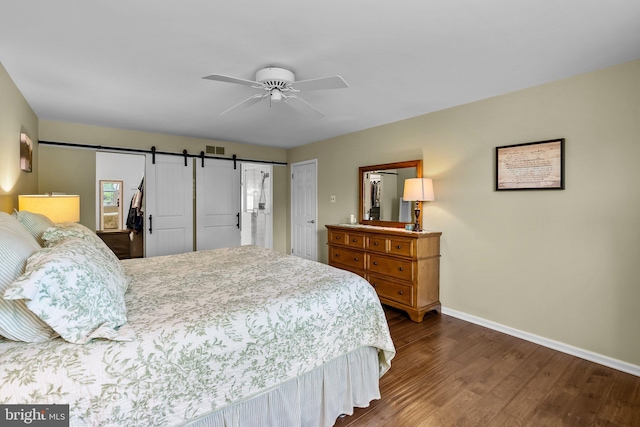 bedroom with a ceiling fan, dark wood finished floors, visible vents, a barn door, and baseboards