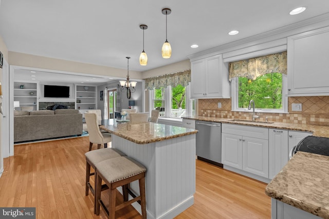 kitchen featuring dishwasher, a sink, open floor plan, light wood-style floors, and white cabinets