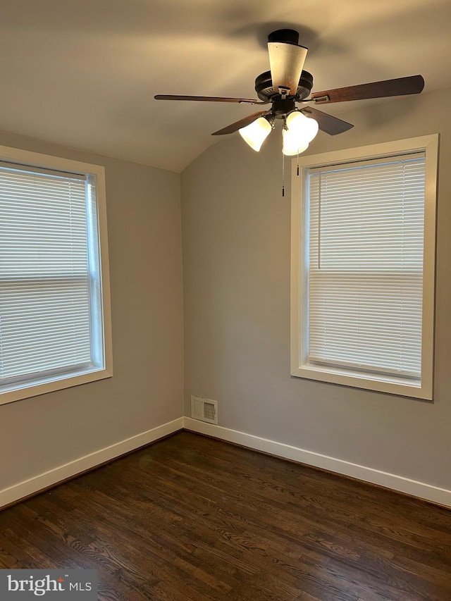 spare room featuring ceiling fan, dark wood finished floors, baseboards, lofted ceiling, and visible vents
