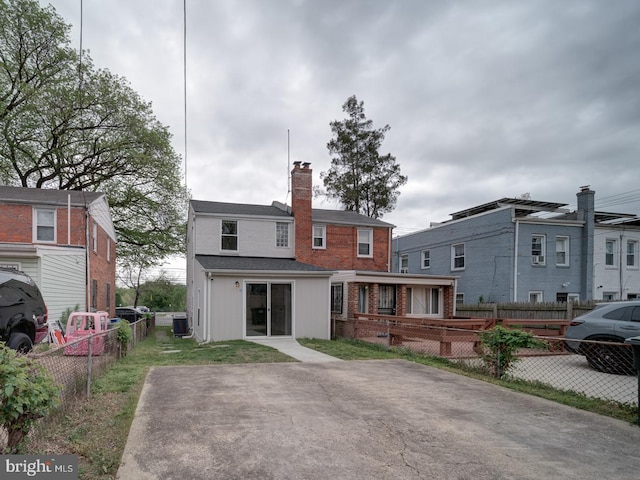 rear view of house featuring a chimney, a deck, central AC unit, brick siding, and fence