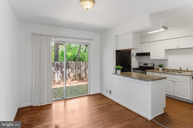 kitchen featuring a peninsula, wood finished floors, stainless steel gas range oven, white cabinetry, and a sink