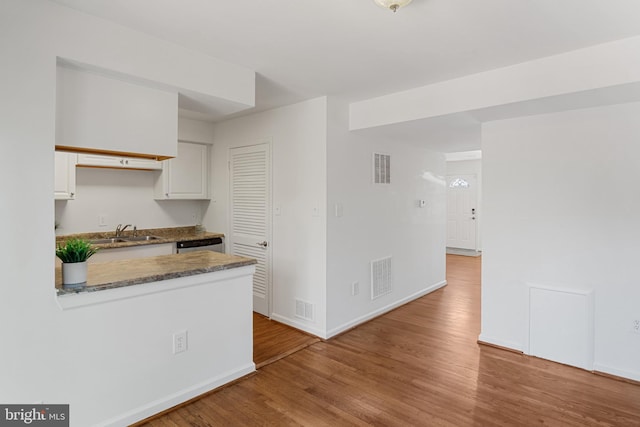 kitchen with a sink, white cabinetry, baseboards, wood finished floors, and visible vents