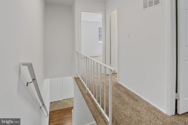 corridor featuring baseboards, an upstairs landing, wood finished floors, and visible vents