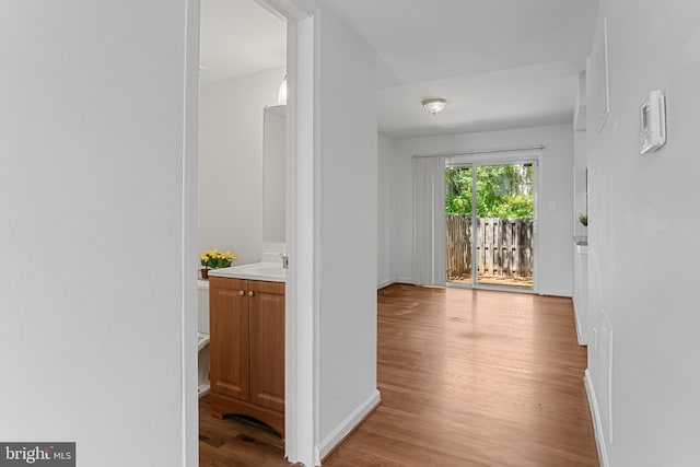 hallway featuring baseboards, a sink, and light wood-type flooring