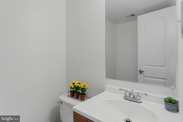 half bathroom with vanity, toilet, and visible vents