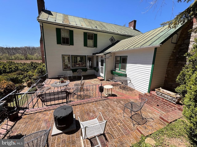 rear view of house featuring metal roof, a patio, a chimney, and a standing seam roof