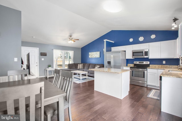 kitchen with vaulted ceiling, a center island, ceiling fan, appliances with stainless steel finishes, and light stone countertops