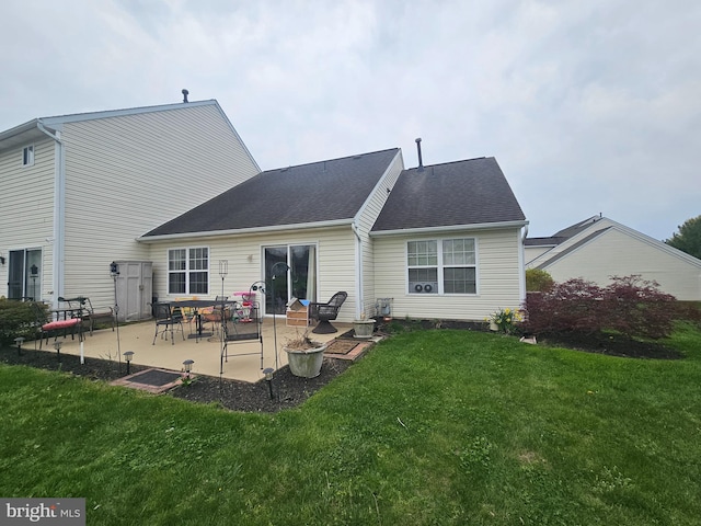back of property with a shingled roof, a patio area, and a yard
