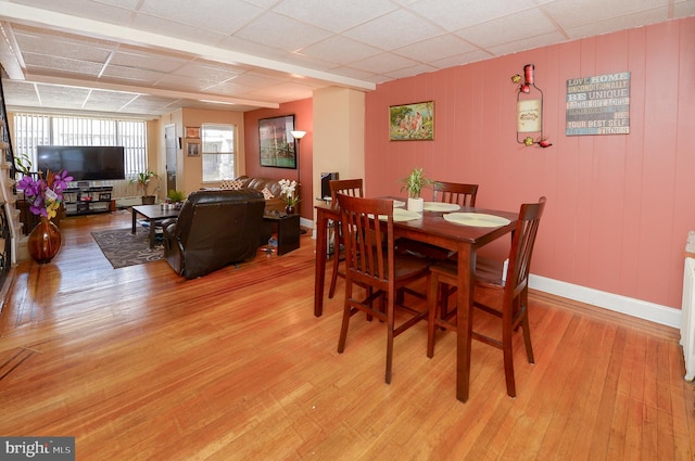 dining area with baseboards, a drop ceiling, and light wood-type flooring