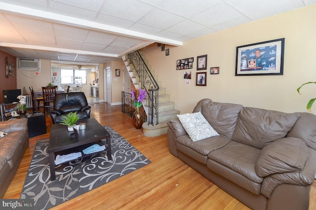 living room featuring wood finished floors, an AC wall unit, stairs, and a drop ceiling