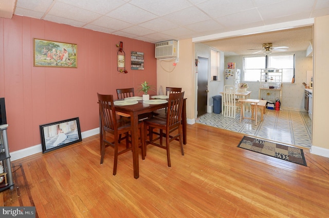 dining space with a wall mounted air conditioner, ceiling fan, baseboards, and wood finished floors