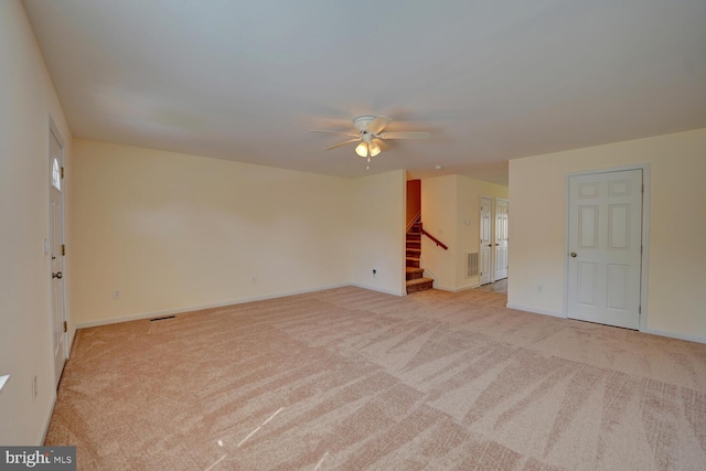 empty room featuring stairway, visible vents, baseboards, light carpet, and a ceiling fan