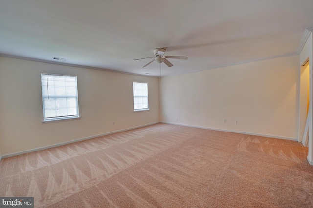 spare room with ceiling fan, visible vents, baseboards, ornamental molding, and light colored carpet