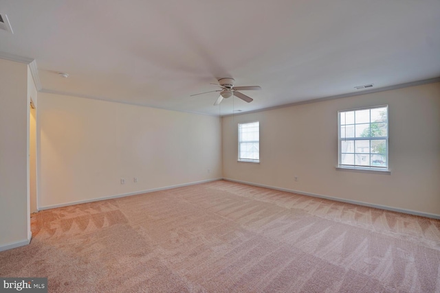 spare room with crown molding, light colored carpet, visible vents, baseboards, and a ceiling fan