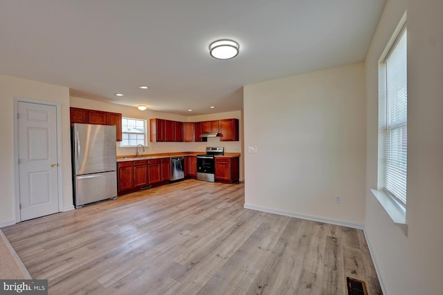 kitchen featuring a sink, stainless steel appliances, light wood-style floors, under cabinet range hood, and visible vents