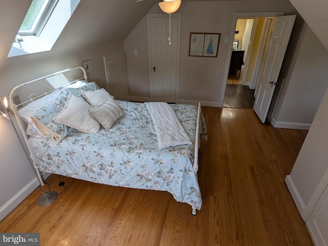bedroom featuring lofted ceiling with skylight, wood finished floors, and baseboards