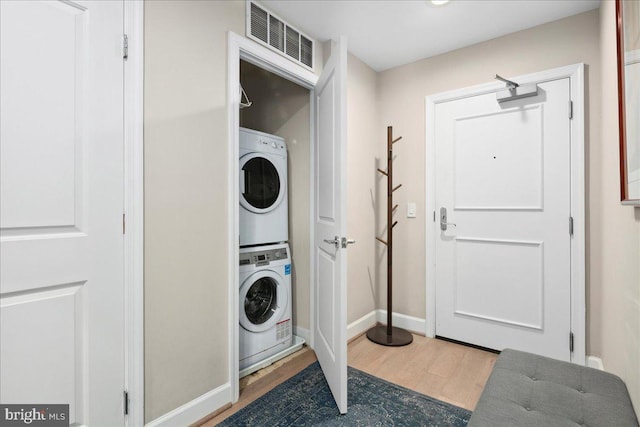clothes washing area with visible vents, baseboards, wood finished floors, stacked washer and clothes dryer, and laundry area