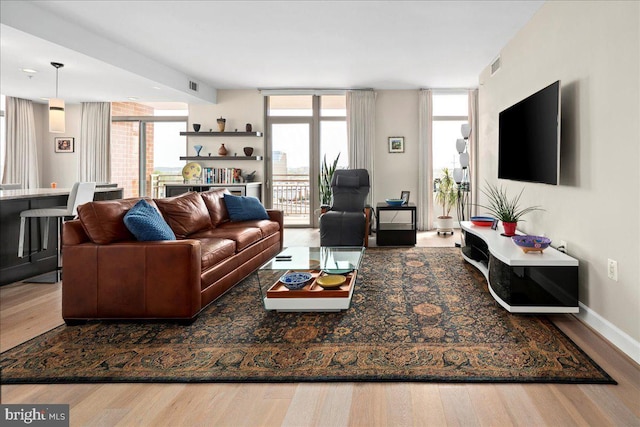 living room with floor to ceiling windows, wood finished floors, visible vents, and plenty of natural light