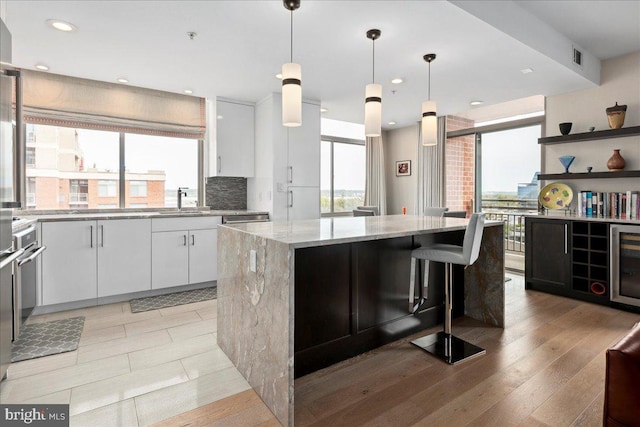 kitchen with light stone counters, a sink, decorative light fixtures, a center island, and white cabinetry