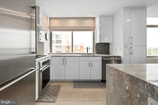 kitchen with light stone counters, appliances with stainless steel finishes, white cabinetry, and a sink