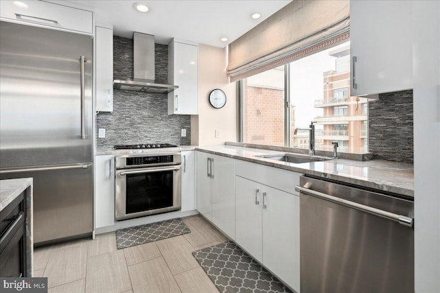kitchen with a sink, white cabinetry, backsplash, wall chimney range hood, and appliances with stainless steel finishes