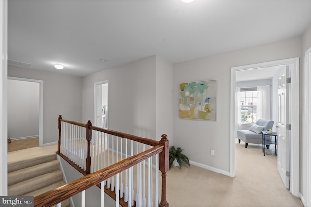 corridor with light colored carpet, baseboards, and an upstairs landing