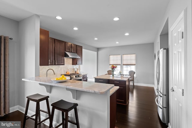 kitchen featuring decorative backsplash, a center island, a peninsula, under cabinet range hood, and stainless steel appliances