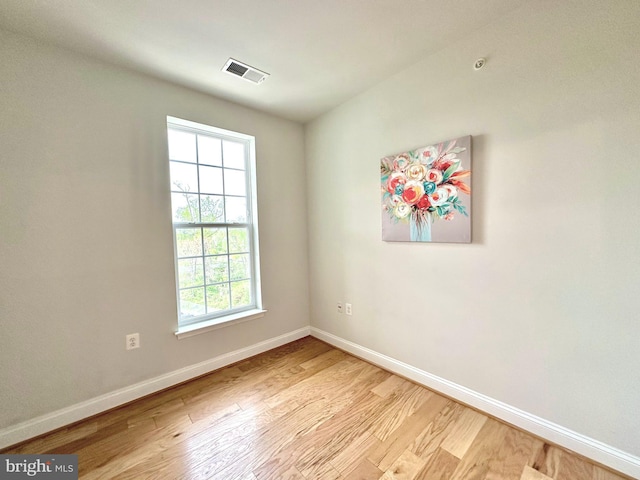 empty room with wood finished floors, visible vents, and baseboards