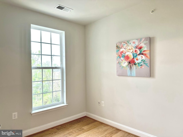 spare room with light wood-type flooring, a wealth of natural light, visible vents, and baseboards
