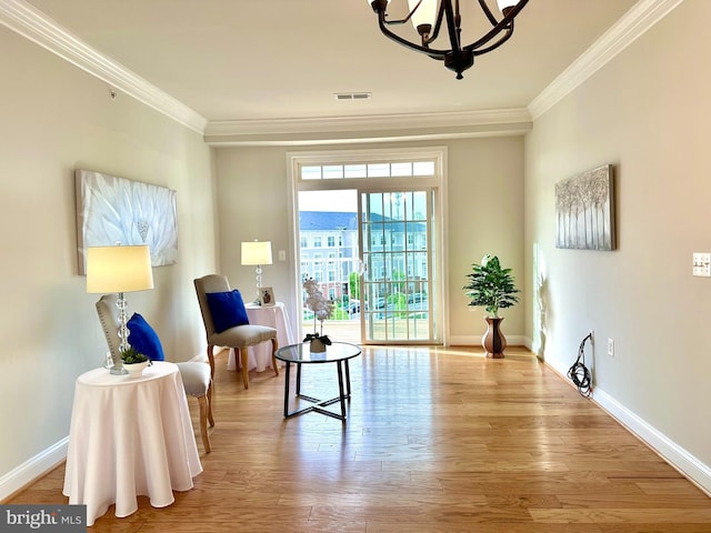 living area with wood finished floors, an inviting chandelier, baseboards, ornamental molding, and visible vents