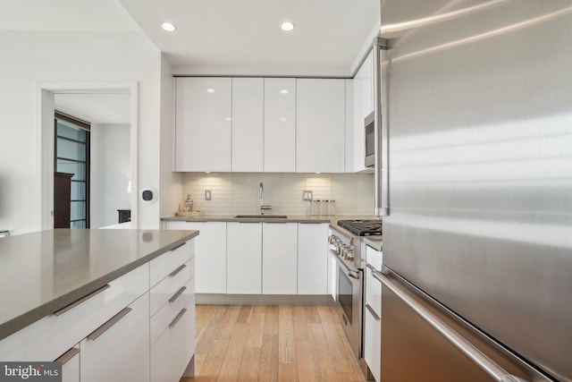 kitchen with premium appliances, light wood finished floors, white cabinetry, backsplash, and modern cabinets