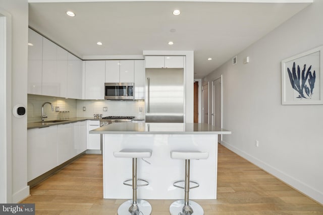 kitchen with a sink, stainless steel appliances, backsplash, white cabinets, and modern cabinets