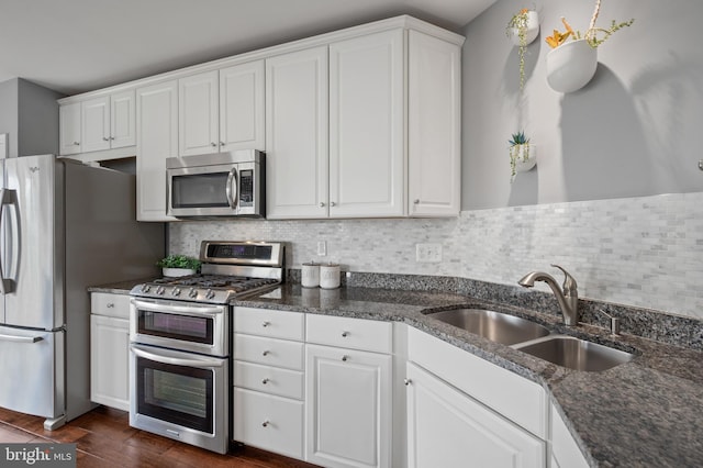 kitchen with appliances with stainless steel finishes, a sink, white cabinetry, tasteful backsplash, and dark stone counters
