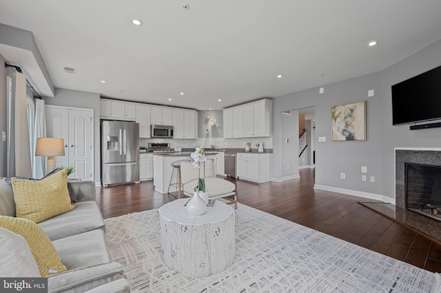 living area featuring dark wood-style flooring, baseboards, a fireplace, recessed lighting, and stairway