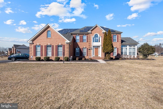view of front of home with brick siding, roof mounted solar panels, and a front lawn
