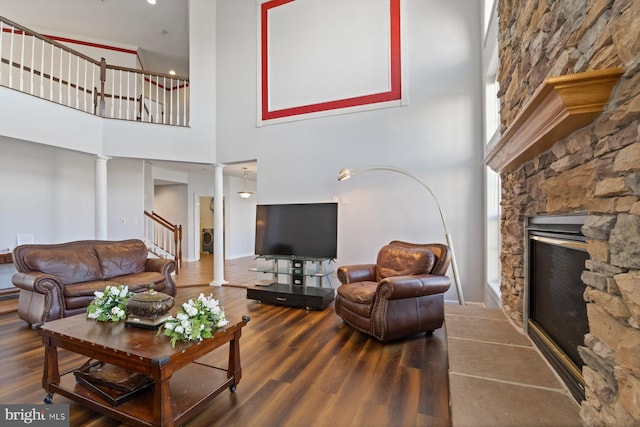living area featuring a stone fireplace, a towering ceiling, wood finished floors, and decorative columns