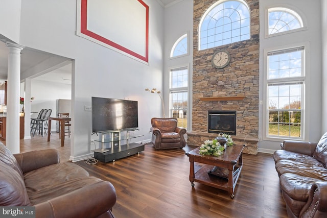 living area with a high ceiling, wood finished floors, baseboards, decorative columns, and a fireplace