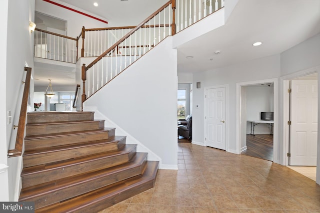 staircase featuring recessed lighting, a healthy amount of sunlight, tile patterned floors, and a high ceiling