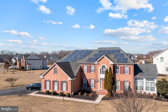 view of front of home with brick siding, solar panels, a shingled roof, and a residential view