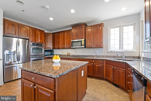 kitchen with a sink, light tile patterned flooring, a kitchen island, dark stone counters, and appliances with stainless steel finishes
