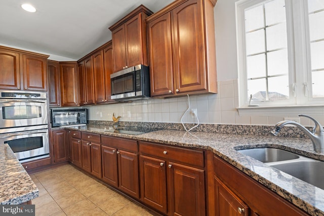 kitchen with a sink, dark stone counters, decorative backsplash, black appliances, and light tile patterned floors