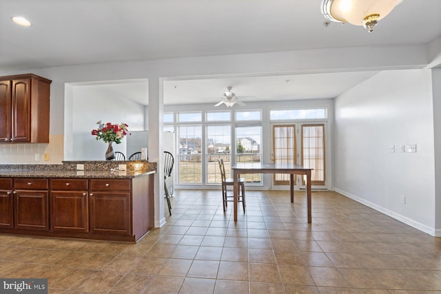 kitchen featuring tile patterned floors, backsplash, a ceiling fan, dark stone counters, and baseboards