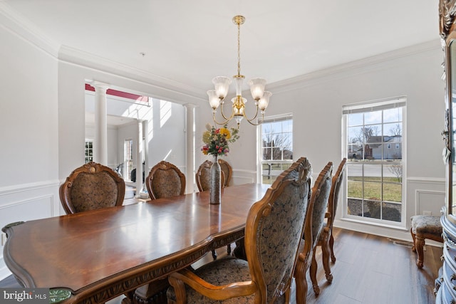dining room featuring ornate columns, a decorative wall, crown molding, wainscoting, and a notable chandelier
