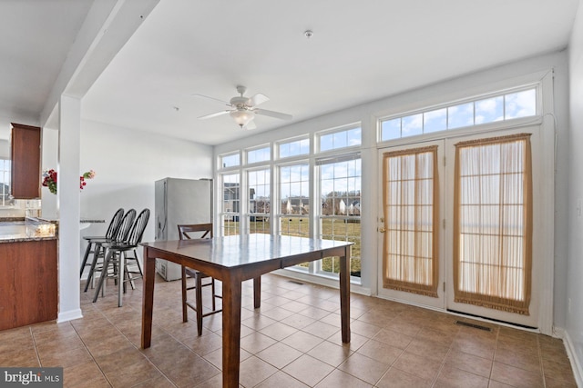 tiled dining space featuring baseboards, a ceiling fan, visible vents, and a wealth of natural light