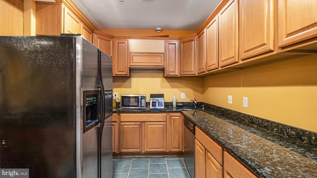 kitchen with stainless steel appliances, dark tile patterned flooring, a sink, and dark stone counters