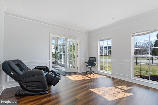 living area featuring wood finished floors, a decorative wall, crown molding, and visible vents