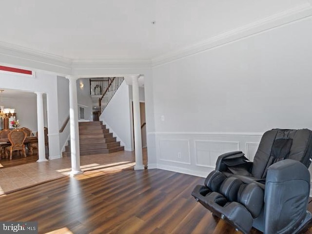 sitting room with ornate columns, crown molding, a chandelier, stairs, and dark wood-style flooring