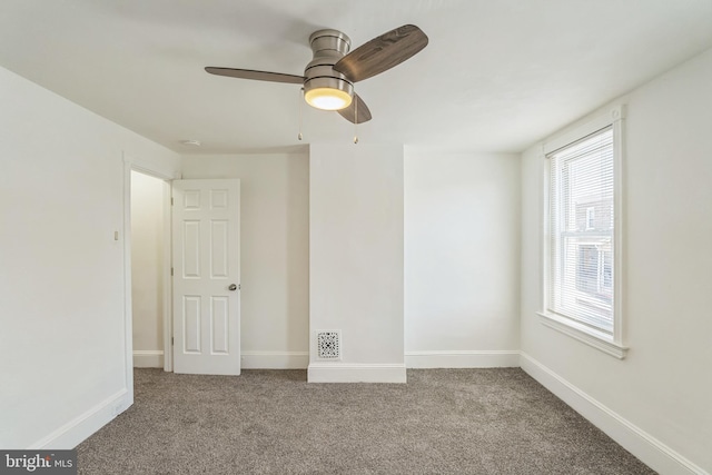 empty room with carpet floors, a ceiling fan, baseboards, and visible vents