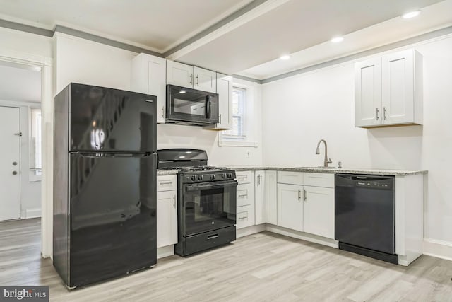 kitchen with ornamental molding, light wood-style floors, white cabinetry, a sink, and black appliances